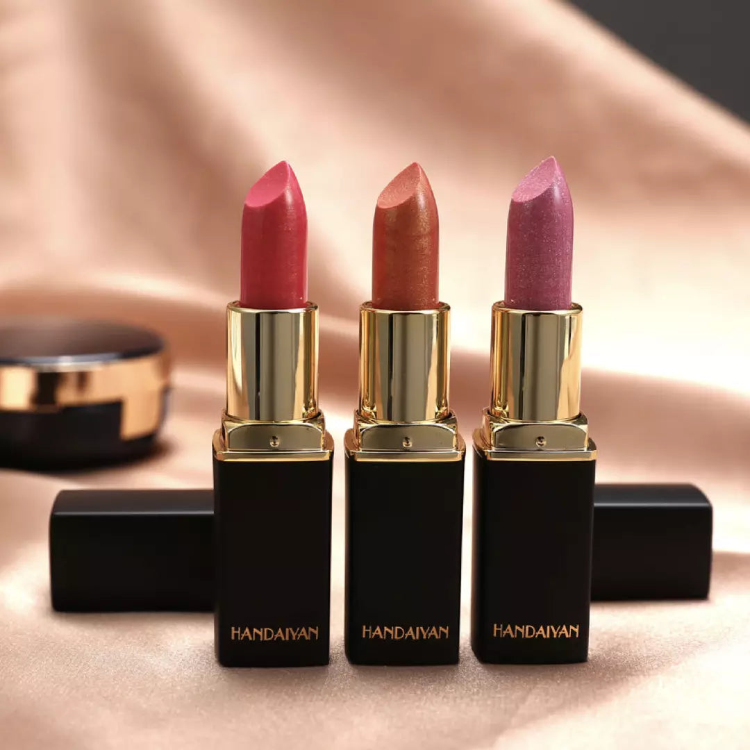 Drie waterproof glitter lipsticks van Handaiyan staan naast elkaar op een zijden doek. De lichtroze, oranje en blush kleurige variant.