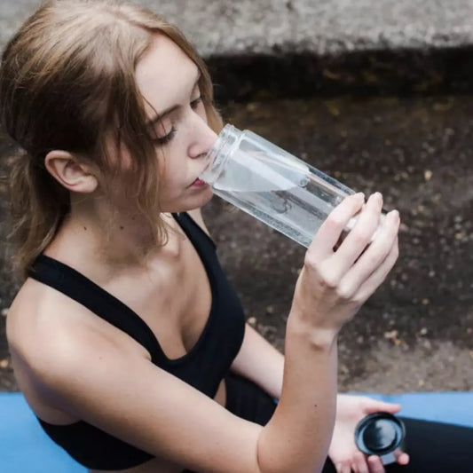 Een dame drinkt uit de zilveren HydroRefresh waterstof fles 2.0. Ze heeft sportkleding aan. 