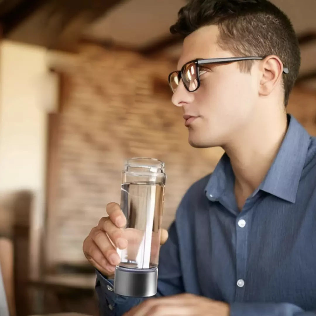  Een zakenman drinkt uit de zilveren HydroRefresh waterstof fles 2.0. Hij zit op kantoor.