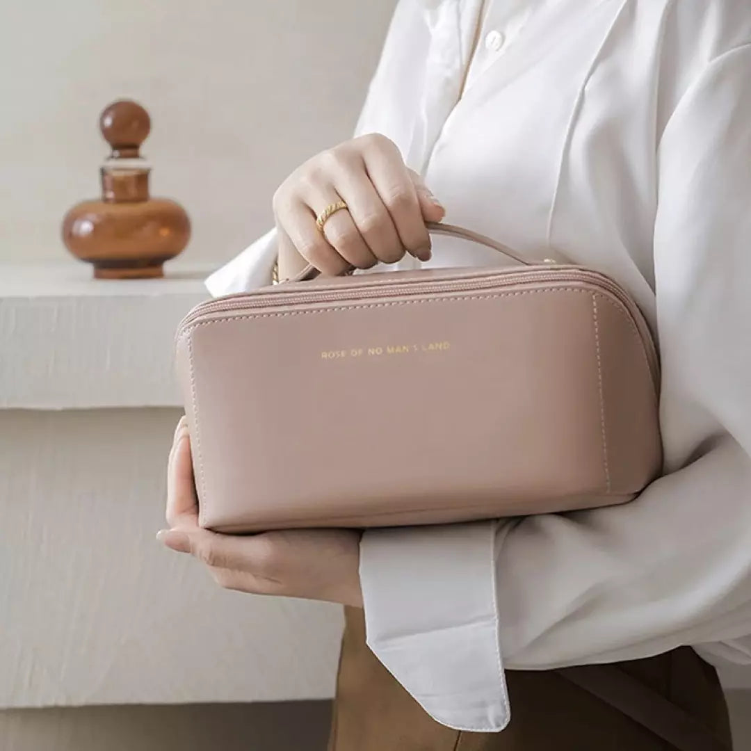 Een vrouw houdt een rose kleurige toilettas vast in haar hand, gevuld met toilet artikelen.